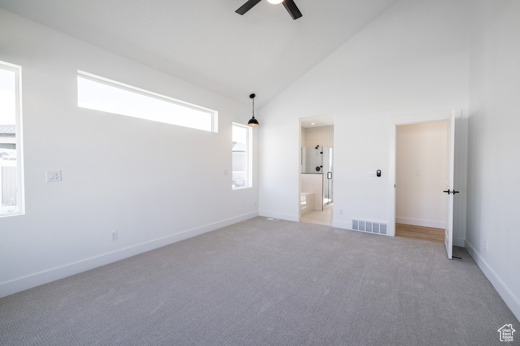 Empty room with a ceiling fan, light colored carpet, and high vaulted ceiling