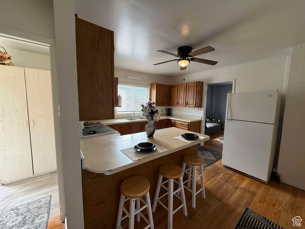 Kitchen with brown cabinetry, light wood-style flooring, a breakfast bar, freestanding refrigerator, and light countertops