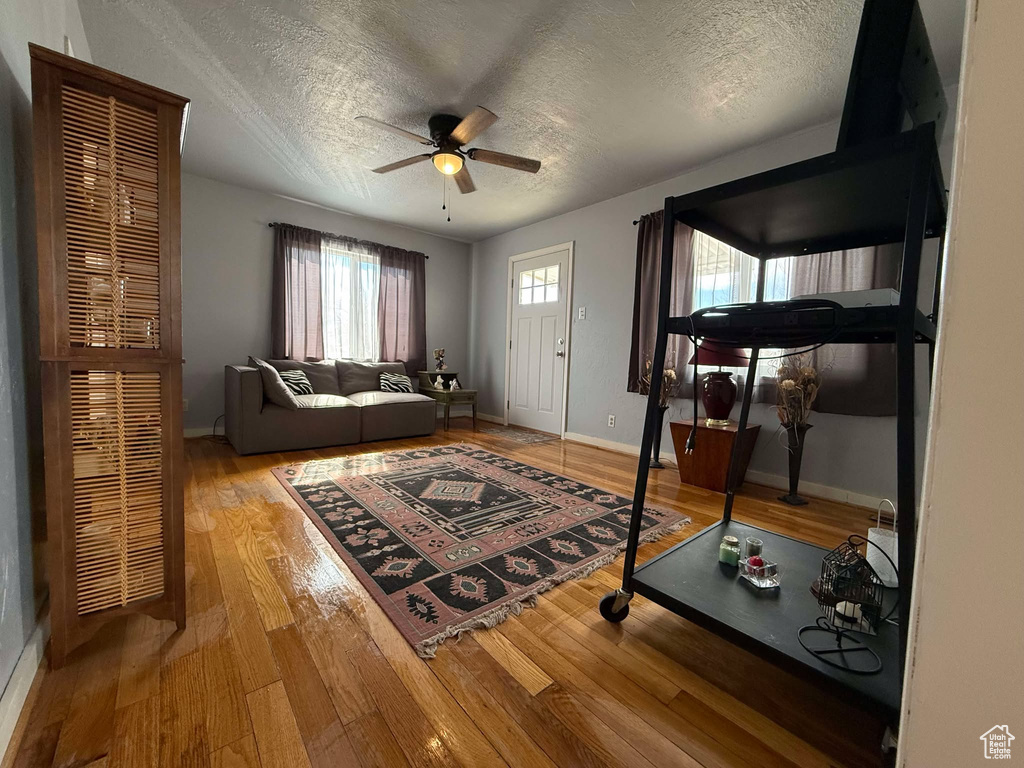 Living room featuring a textured ceiling, wood finished floors, a ceiling fan, and baseboards