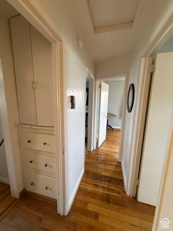 Hallway featuring light wood-style floors, a tray ceiling, and baseboards