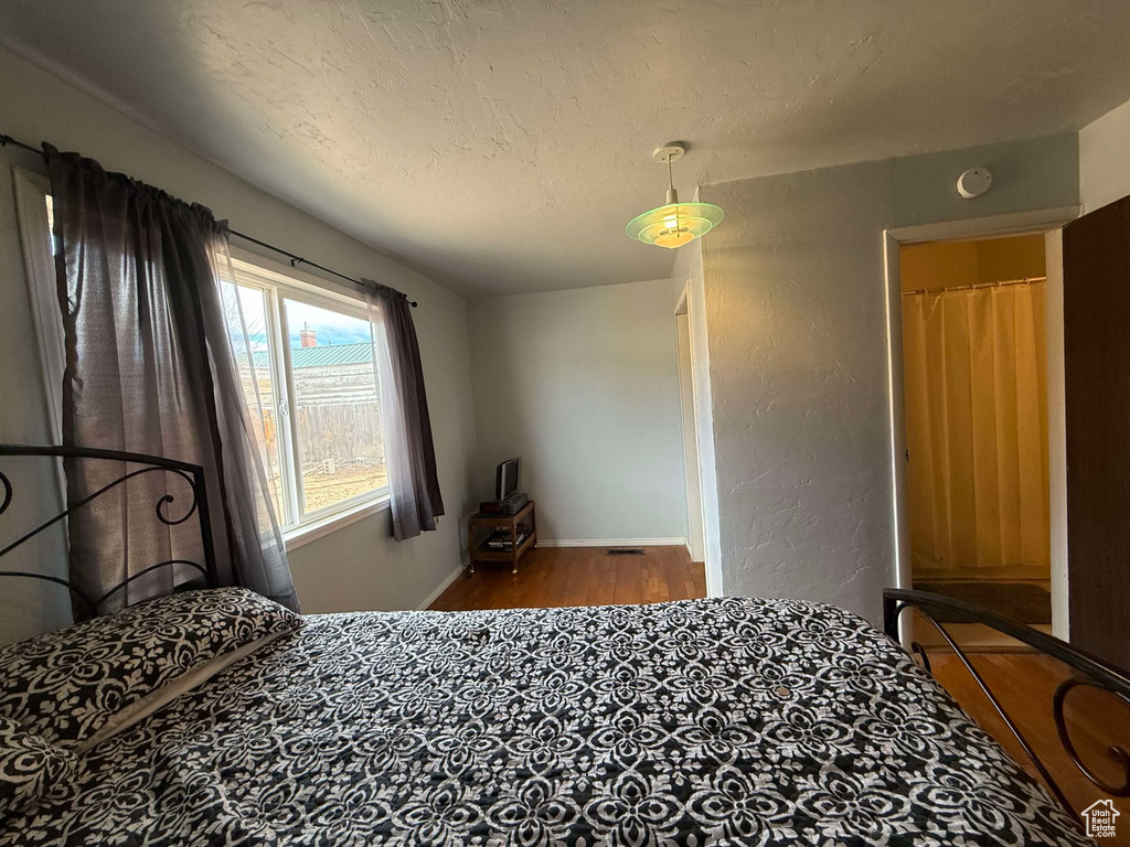 Bedroom featuring a textured wall, a textured ceiling, baseboards, and wood finished floors