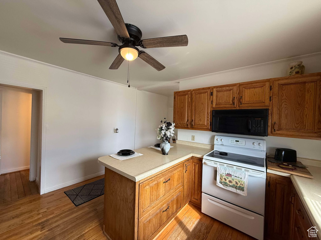 Kitchen with black microwave, a peninsula, electric range, light countertops, and brown cabinetry