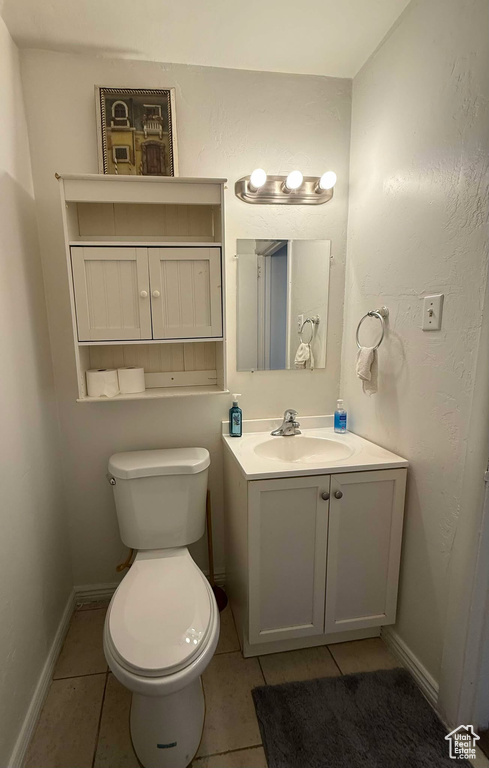 Half bath featuring toilet, vanity, baseboards, and tile patterned floors