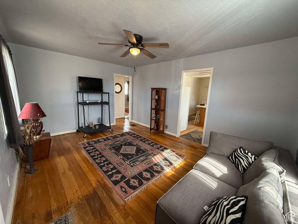 Living area featuring ceiling fan, a textured ceiling, wood finished floors, and baseboards