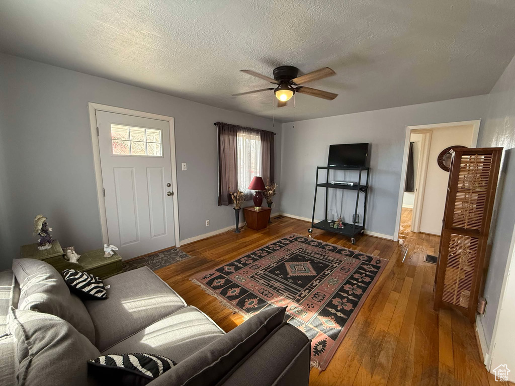 Living area featuring baseboards, visible vents, ceiling fan, wood finished floors, and a textured ceiling