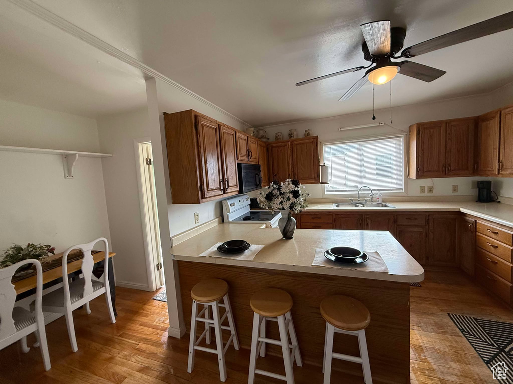 Kitchen with a kitchen bar, black microwave, light countertops, and electric stove