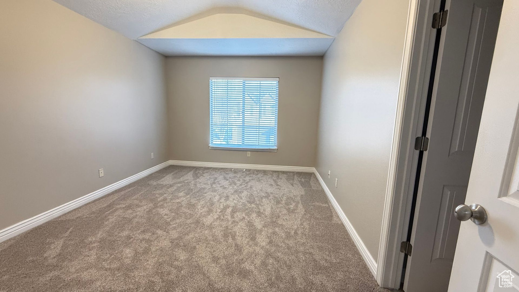 Unfurnished room featuring baseboards, vaulted ceiling, and light colored carpet