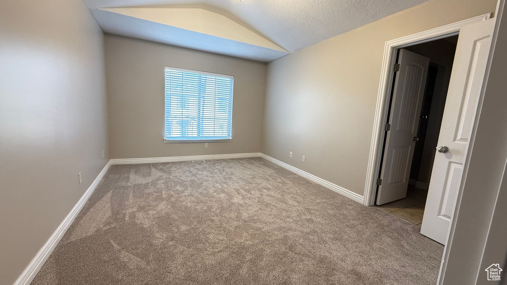 Unfurnished room with vaulted ceiling, a textured ceiling, baseboards, and light colored carpet