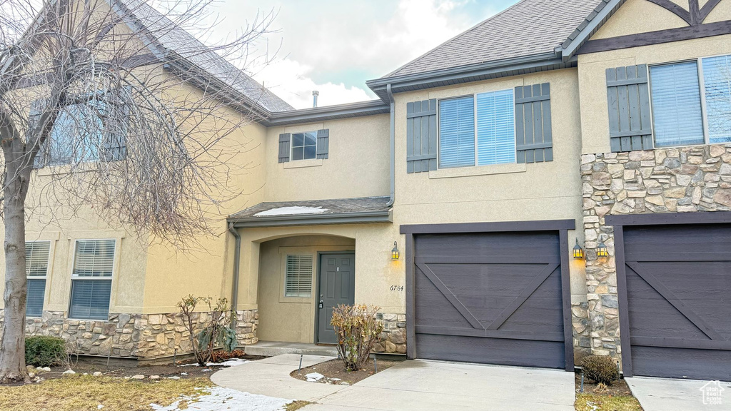 Townhome / multi-family property featuring an attached garage, stone siding, concrete driveway, and stucco siding