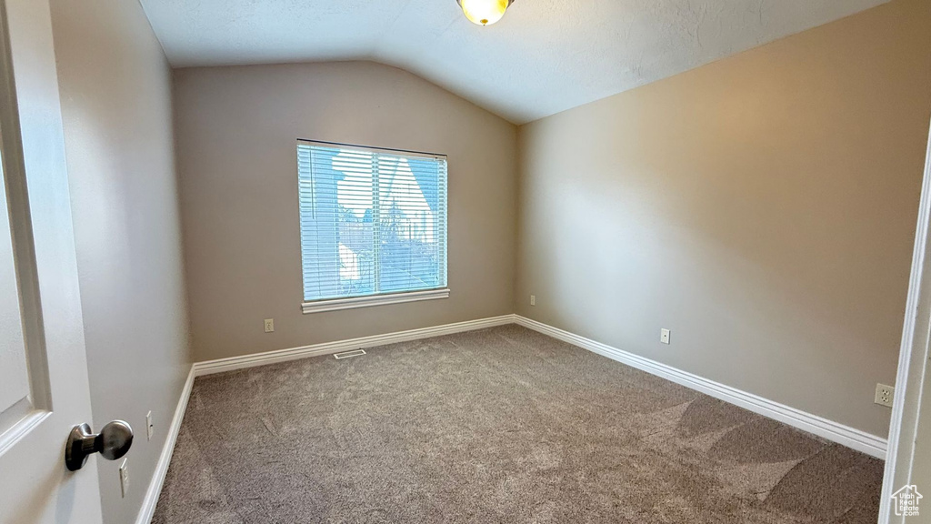 Carpeted spare room with visible vents, baseboards, and vaulted ceiling