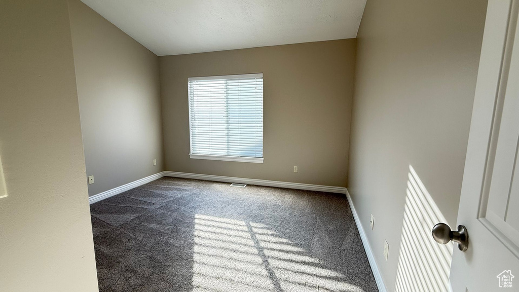 Empty room featuring dark colored carpet and baseboards