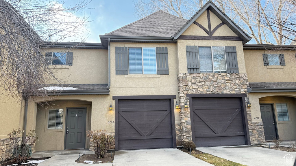 View of front facade featuring stone siding, roof with shingles, concrete driveway, and stucco siding