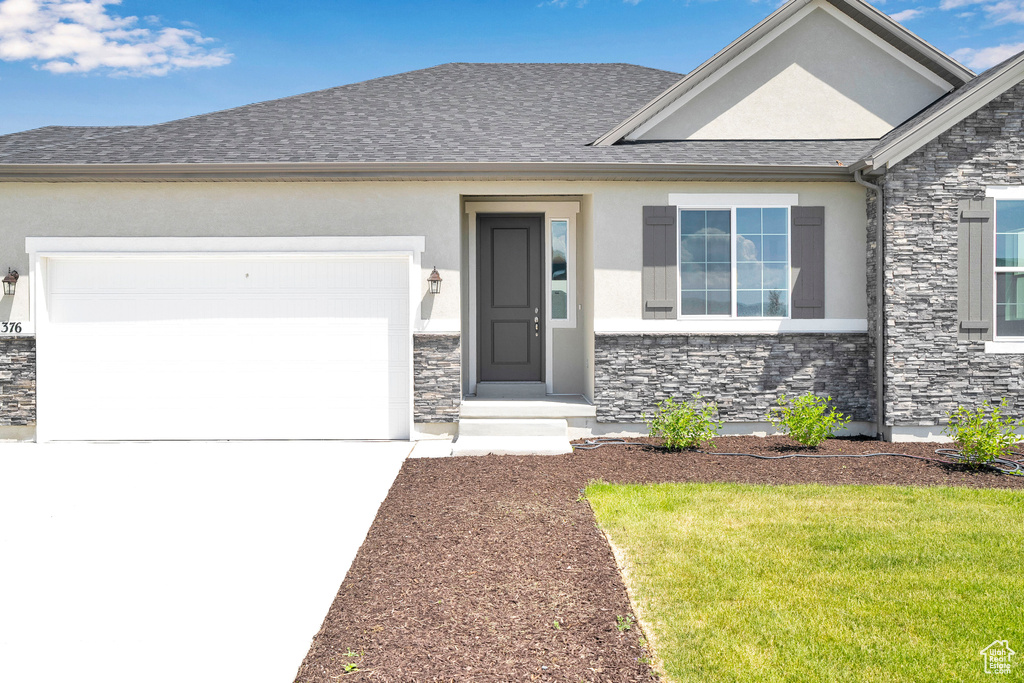 View of front facade featuring stone siding, stucco siding, concrete driveway, an attached garage, and a front yard