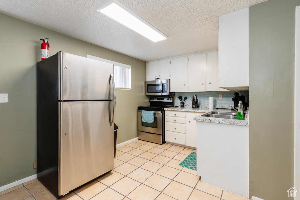 Kitchen with light tile patterned flooring, stainless steel appliances, a sink, white cabinetry, and light countertops