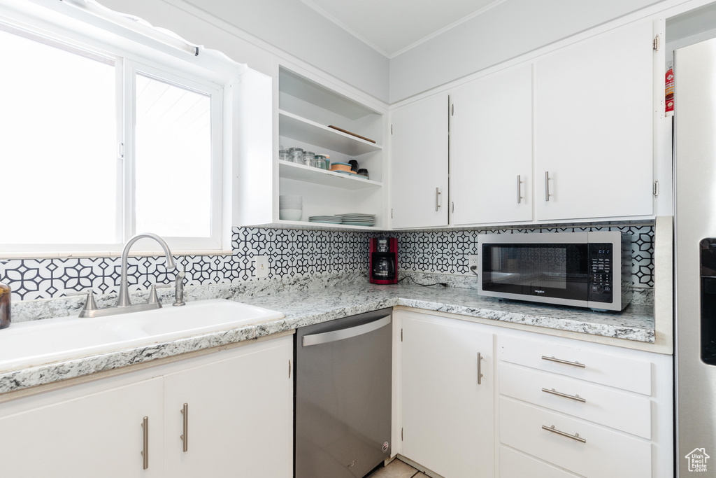 Kitchen with tasteful backsplash, white cabinets, light countertops, and dishwasher