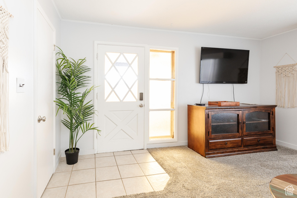 Foyer featuring light colored carpet, crown molding, and light tile patterned floors