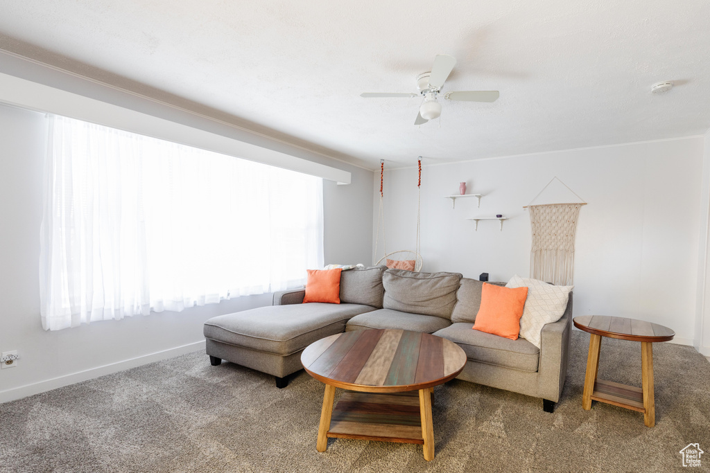 Carpeted living room featuring a ceiling fan and baseboards