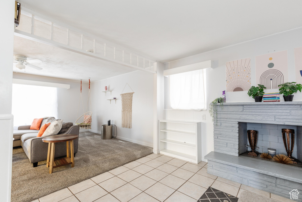 Living room with light carpet, light tile patterned floors, a fireplace, and a ceiling fan