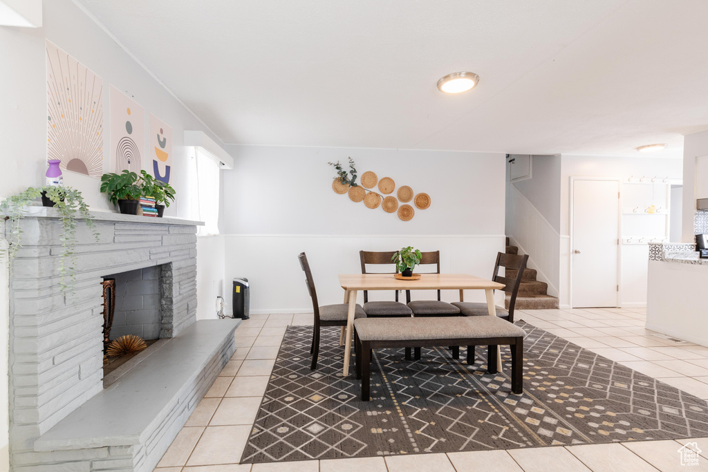 Dining area with stairs, a fireplace with raised hearth, and light tile patterned floors