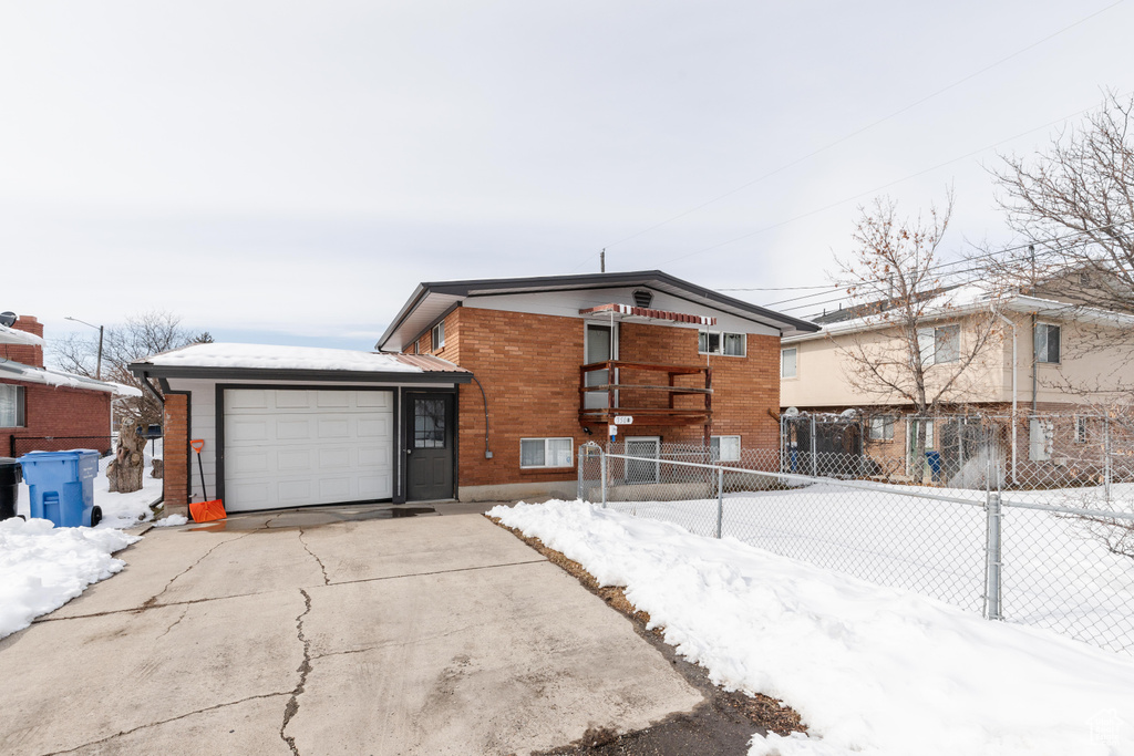 View of front of house featuring a garage, fence, concrete driveway, and brick siding