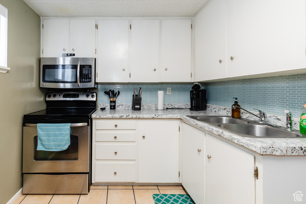 Kitchen featuring stainless steel appliances, light countertops, decorative backsplash, white cabinets, and a sink