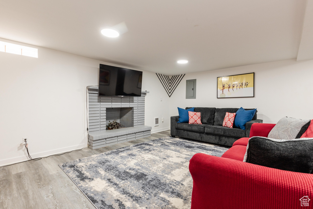 Living area featuring electric panel, baseboards, light wood-type flooring, a brick fireplace, and recessed lighting