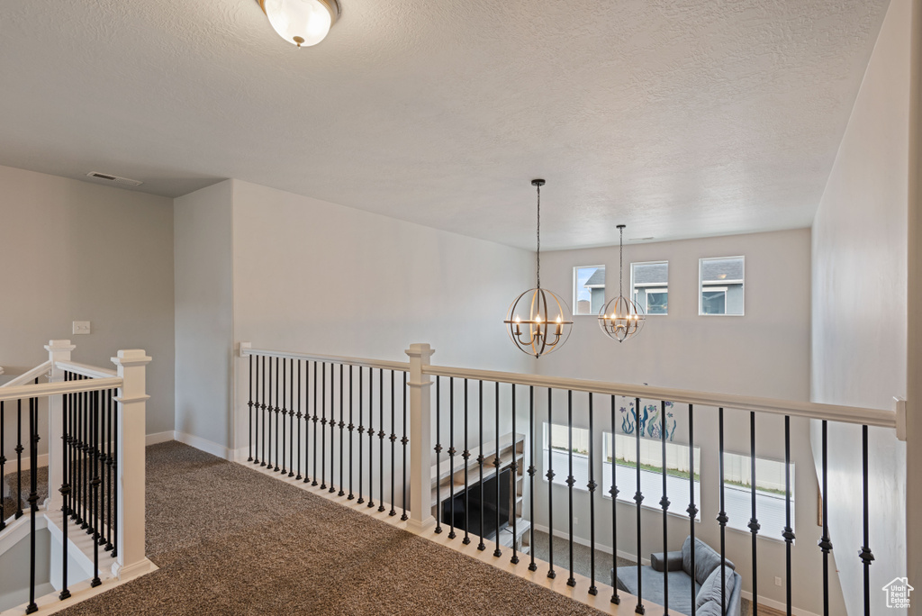 Hallway featuring a textured ceiling, carpet flooring, visible vents, an upstairs landing, and an inviting chandelier