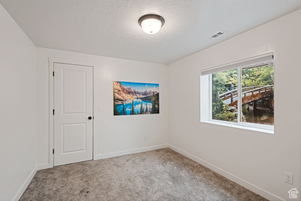 Carpeted spare room with visible vents, a textured ceiling, and baseboards