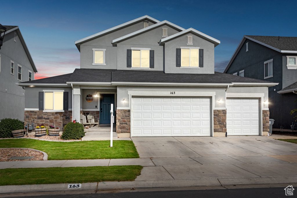 View of front of home with stone siding, a shingled roof, concrete driveway, and stucco siding