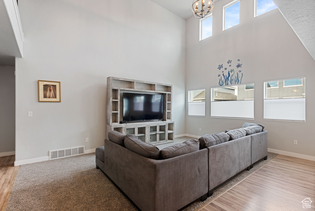 Living room with a notable chandelier, a towering ceiling, baseboards, visible vents, and light wood finished floors