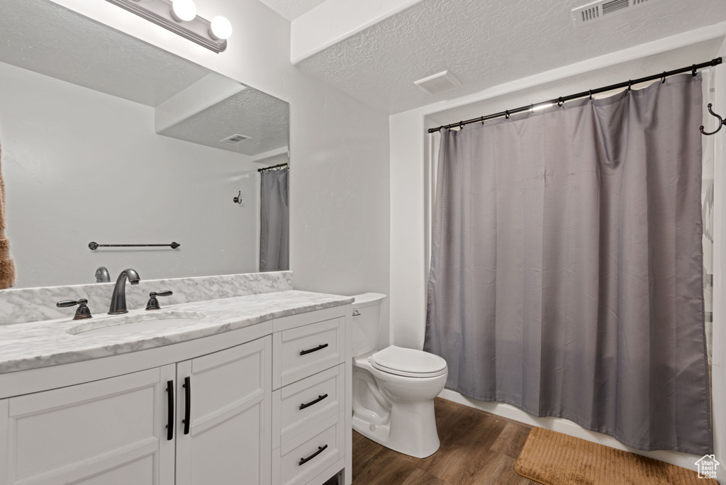 Full bathroom with a textured ceiling, toilet, wood finished floors, visible vents, and vanity
