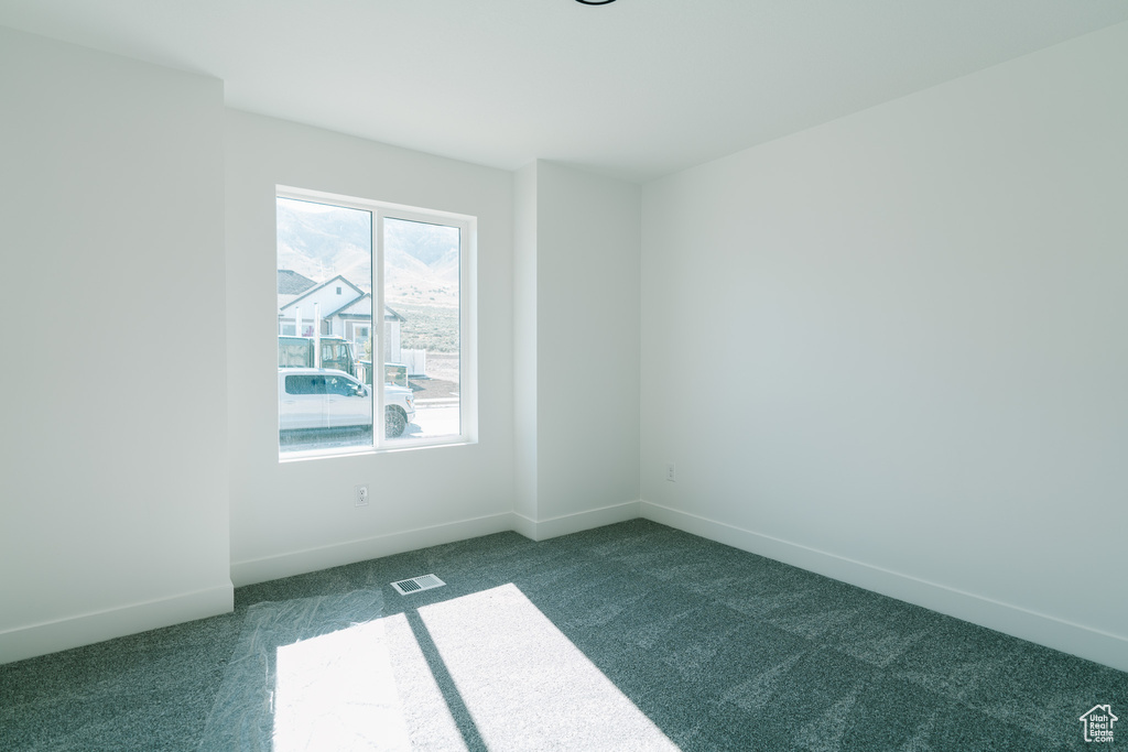 Empty room with baseboards, dark colored carpet, and visible vents