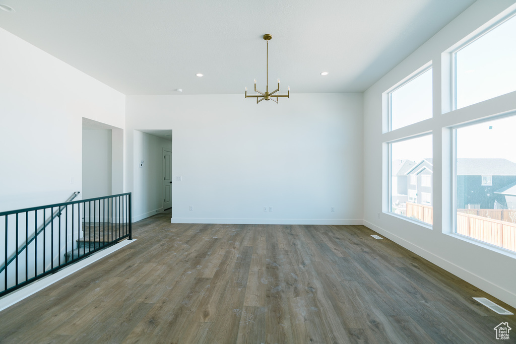 Unfurnished room with baseboards, wood finished floors, a notable chandelier, and visible vents