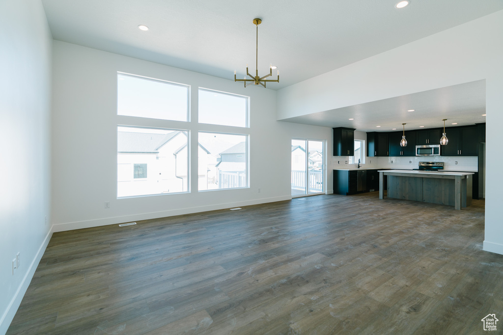 Unfurnished living room featuring an inviting chandelier, recessed lighting, baseboards, and dark wood-style floors