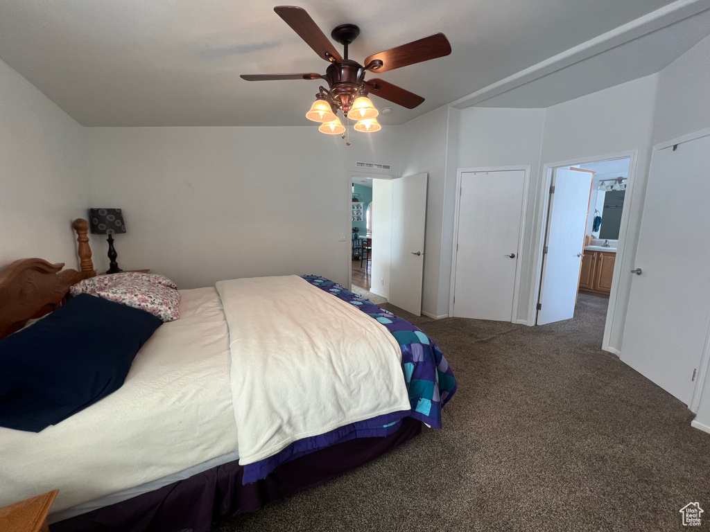 Bedroom with visible vents, dark colored carpet, ensuite bath, and a ceiling fan