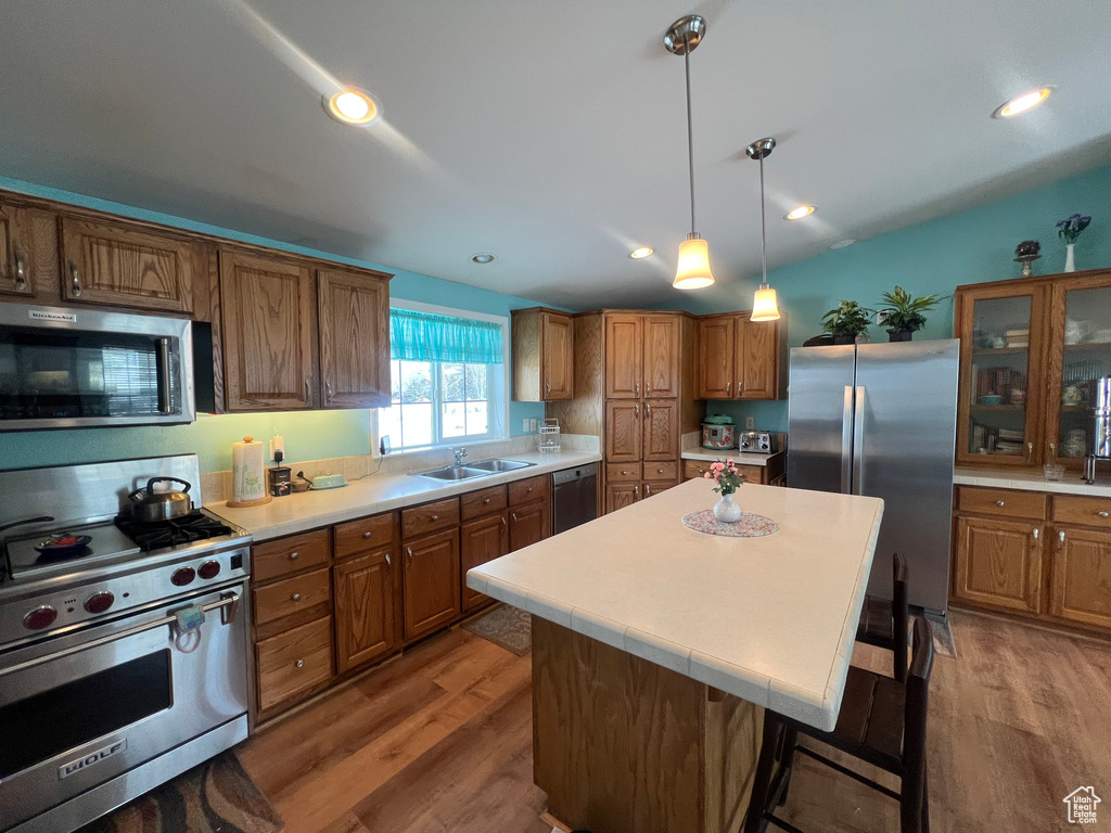 Kitchen with light countertops, appliances with stainless steel finishes, a kitchen island, and glass insert cabinets