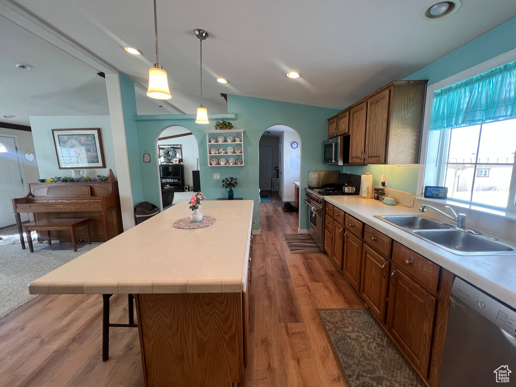 Kitchen featuring arched walkways, decorative light fixtures, light countertops, stainless steel appliances, and a sink