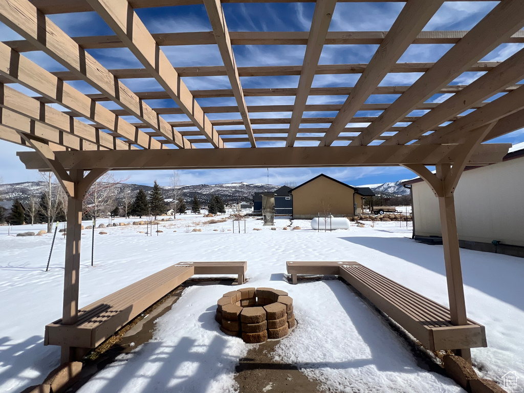 Snow covered patio featuring an outdoor fire pit, a mountain view, and a pergola