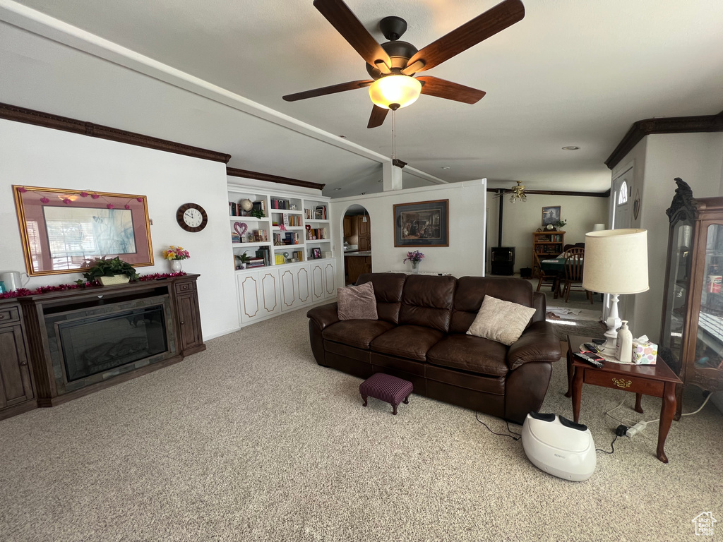 Carpeted living area featuring arched walkways, lofted ceiling, a ceiling fan, ornamental molding, and a glass covered fireplace