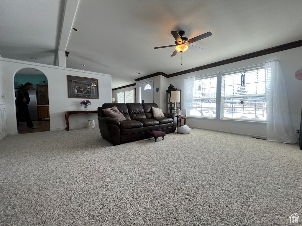 Carpeted living area featuring arched walkways, ornamental molding, and a ceiling fan