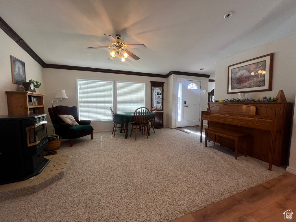 Interior space with a wood stove, ceiling fan, ornamental molding, and light colored carpet