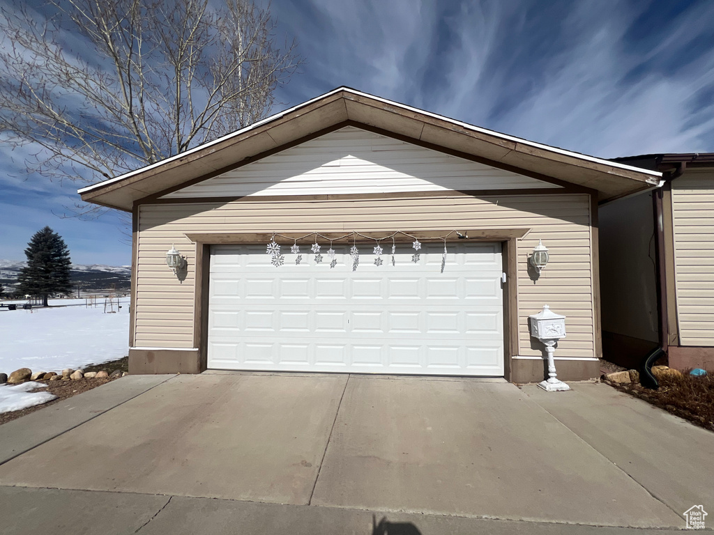 Snow covered garage featuring concrete driveway