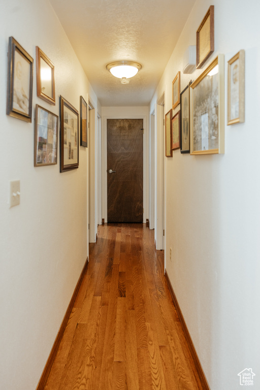 Corridor with baseboards, wood finished floors, and a textured ceiling