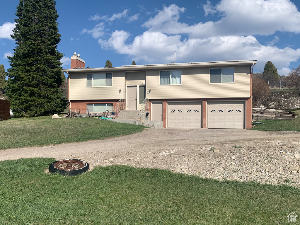 Bi-level home with a chimney, driveway, a fire pit, an attached garage, and a front yard