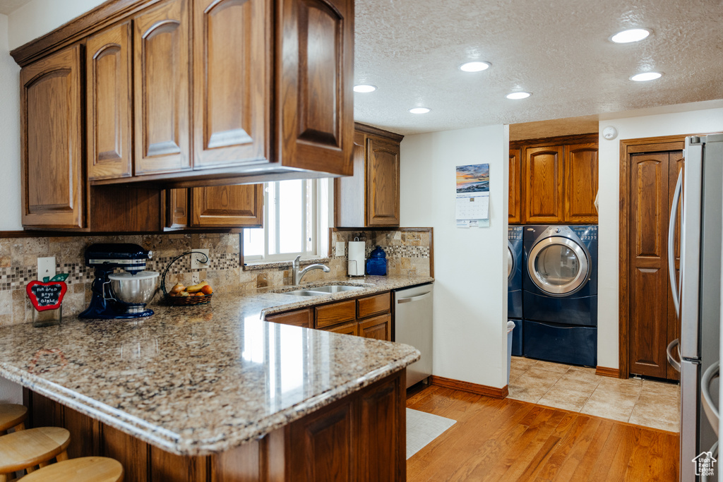 Kitchen with recessed lighting, a peninsula, washing machine and dryer, appliances with stainless steel finishes, and a sink