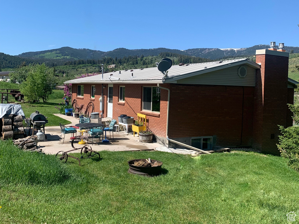 Back of house featuring a patio, a lawn, a mountain view, a chimney, and brick siding