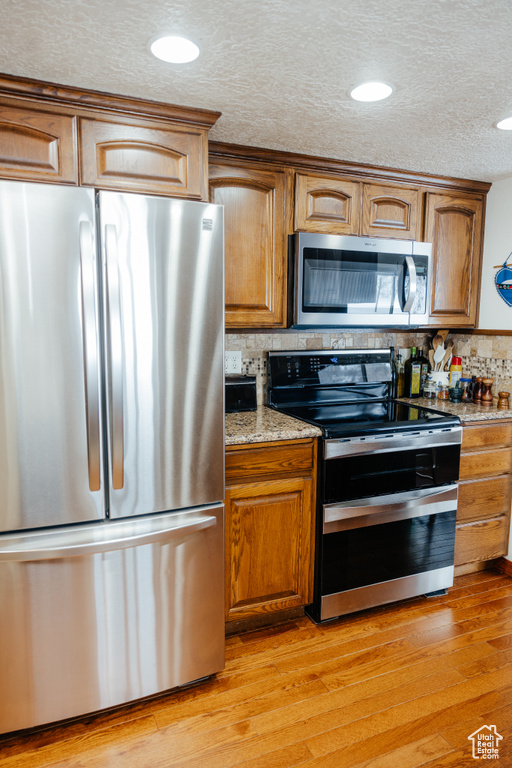 Kitchen featuring brown cabinets, decorative backsplash, appliances with stainless steel finishes, and light wood-style flooring