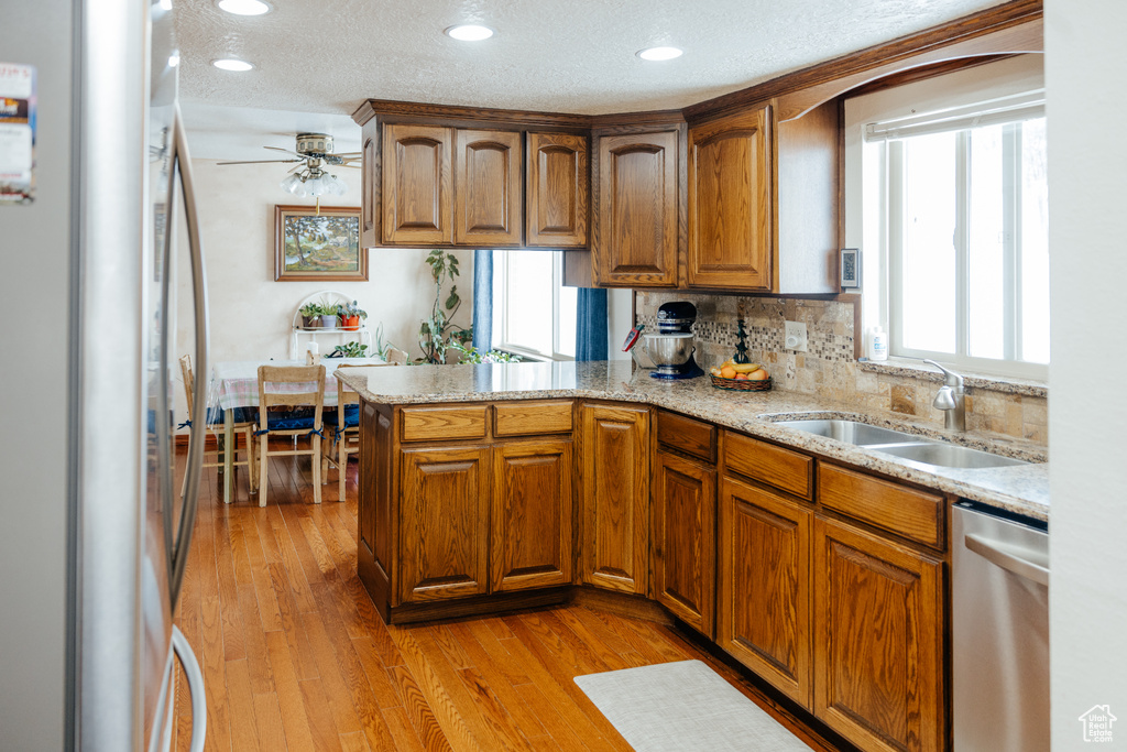 Kitchen featuring light wood-style floors, a peninsula, a sink, stainless steel appliances, and brown cabinets