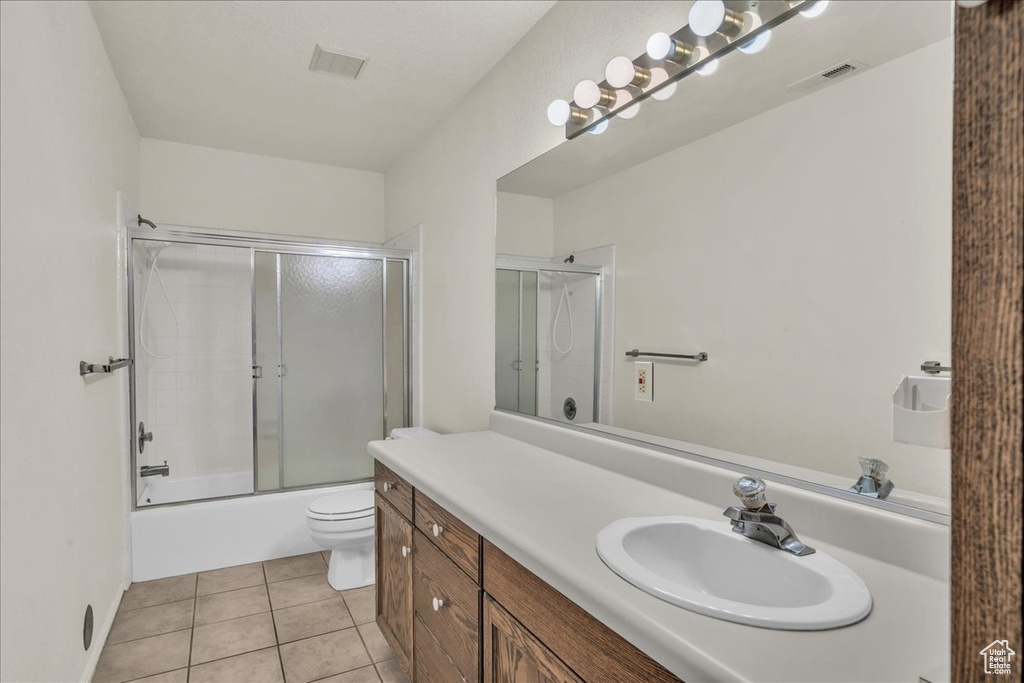 Bathroom with tile patterned floors, vanity, toilet, and bath / shower combo with glass door