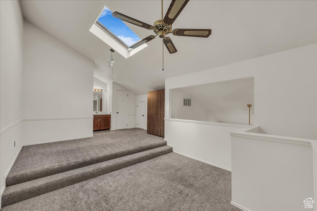 Carpeted spare room featuring a ceiling fan, a skylight, lofted ceiling, and baseboards